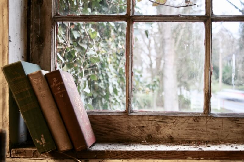 A Worn window frame with 3 old books of a shelf.