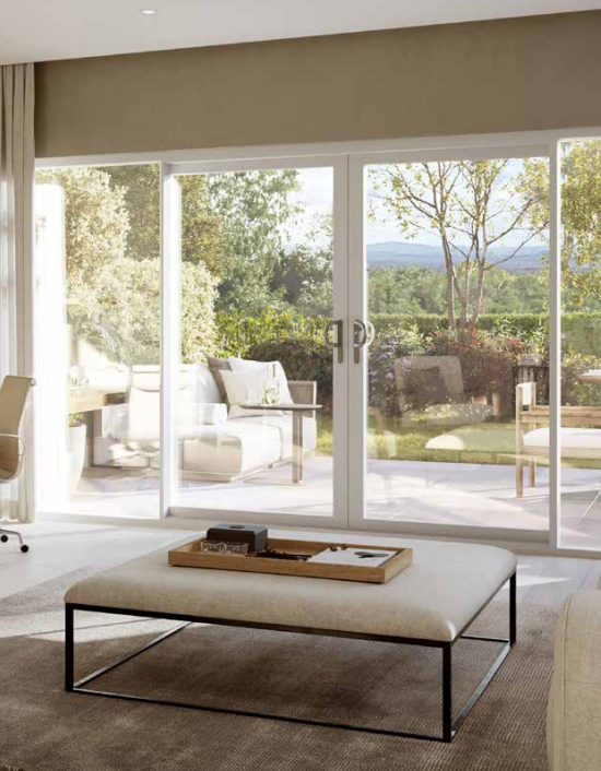 A stellar sliding patio door, made using aluminium materials. This door leads to the garden, and has a white finish. From the interior of the door, you can see a table, with a very green garden on display through the glass. 