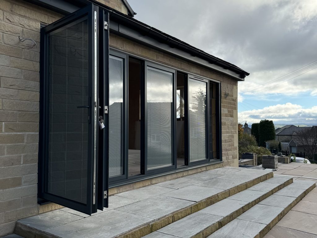 Quickslide's aluminium slide and fold doors, at the top of an outdoor stairway. These doors are black, and partly open 