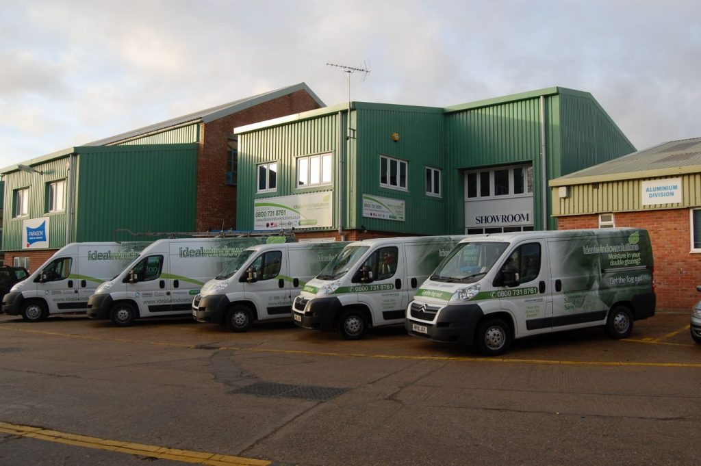 fleet of five Ideal Window Solutions vans outside showroom