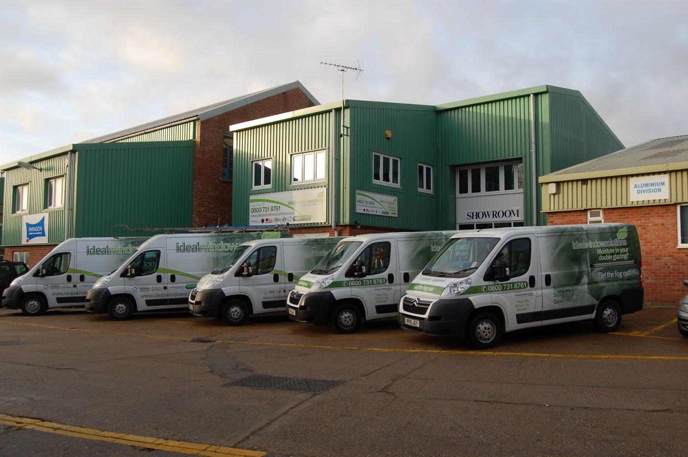 fleet of five Ideal Window Solutions vans outside showroom